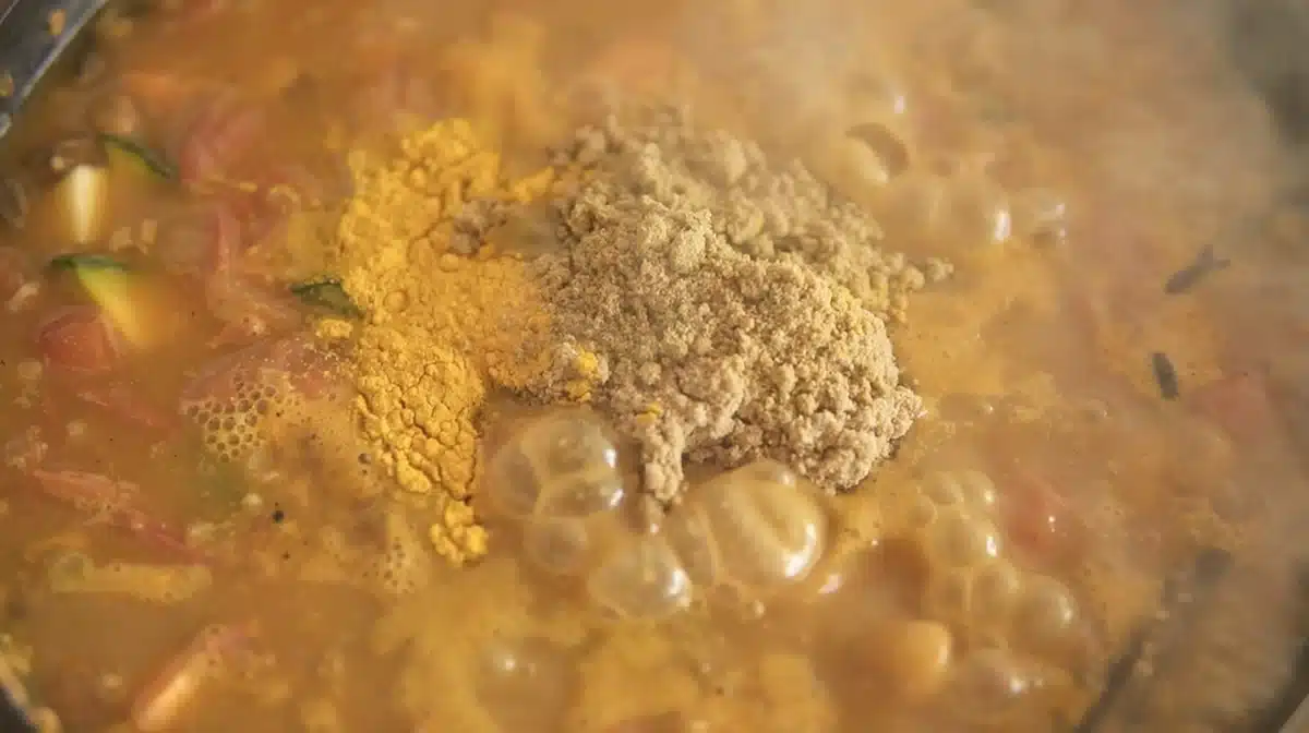 野菜を炒めたフライパンに、パウダースパイスと豆乳ヨーグルトを加えている